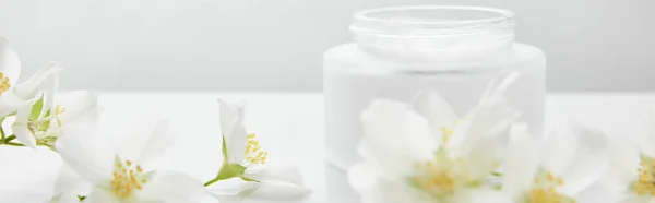 Colpo panoramico di fiori di gelsomino su superficie bianca vicino a vaso con crema — Foto stock