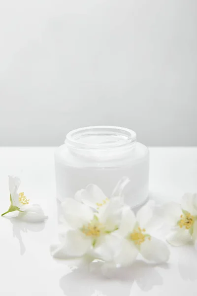 Jasmine flowers on white surface near jar with cream — Stock Photo