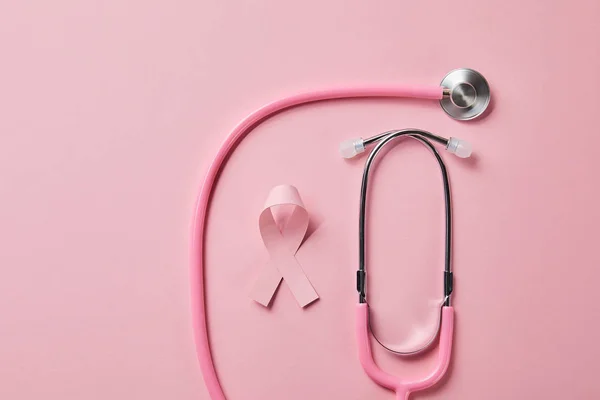 Pink stethoscope and breast cancer ribbon on light pink background — Stock Photo