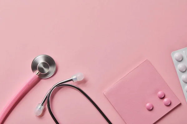 Vue du dessus du stéthoscope rose, trois pilules sur papier et plaquette thermoformée sur fond rose clair — Photo de stock