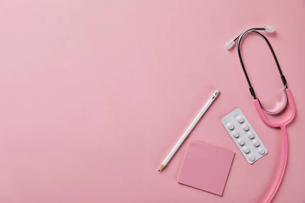 Ansicht von Stethoskop, Bleistift, Papier und Blisterverpackung auf rosa Hintergrund — Stockfoto