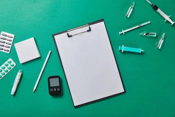 Ansicht von Bleistift auf Mappe mit leerem Papier, abgerundet durch verschiedene medizinische Hilfsmittel auf grüner Oberfläche — Stockfoto