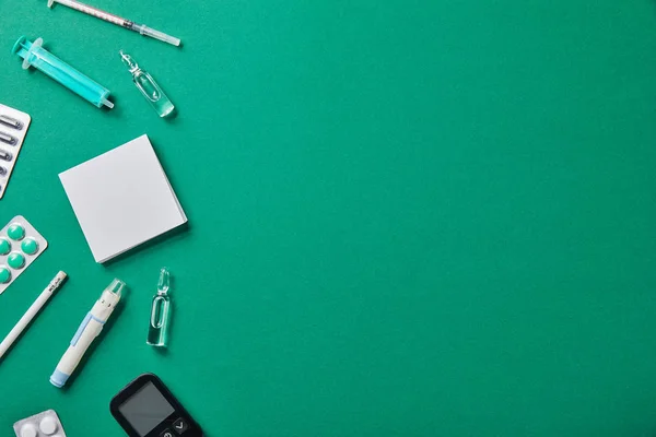 Blister, fiale, lancetta del sangue, glucometro, siringhe, note adesive e matita su sfondo verde — Foto stock