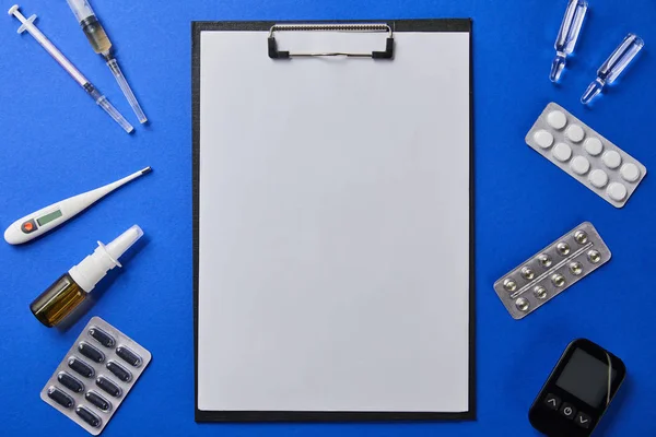 Top view of folder with blank paper rounded by various medical supplies on blue surface — Stock Photo