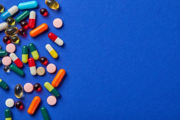 Varias píldoras médicas de colores en la superficie azul - foto de stock