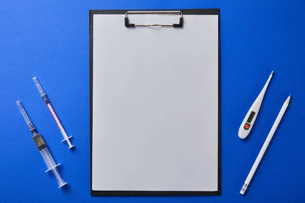 Draufsicht auf Spritzen, Thermometer und Bleistift in der Nähe von Ordnern mit leerem Papier isoliert auf blau — Stockfoto