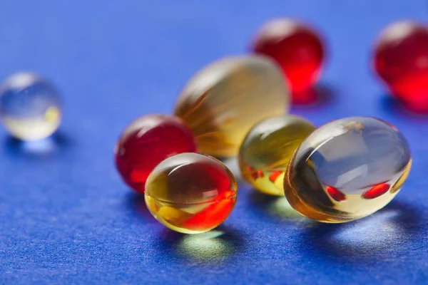 Vista de perto de óleo de peixe e vitaminas E no fundo azul — Fotografia de Stock