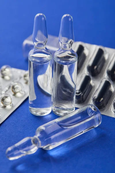 Close up view of blister packs and transparent ampules with medicine on blue — Stock Photo
