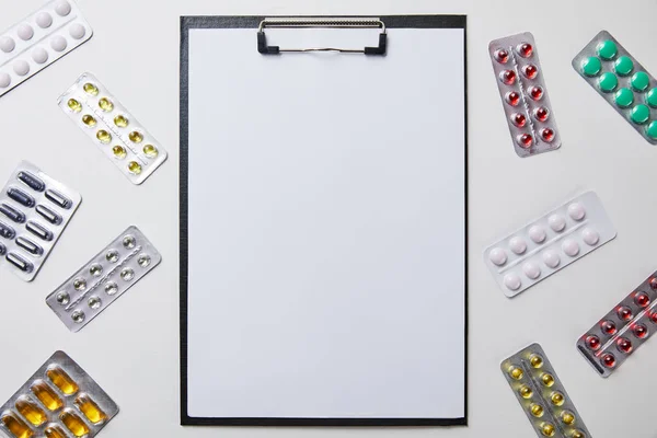 Top view of blister packs around folder with empty paper isolated on white — Stock Photo