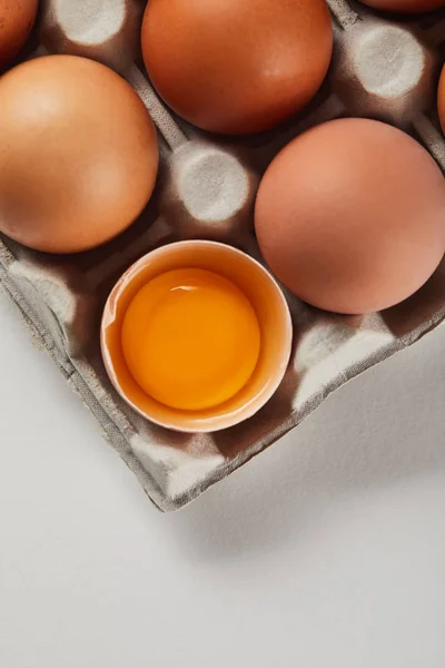 Vista superior de la cáscara de huevo rota con yema amarilla cerca de los huevos en caja de cartón - foto de stock