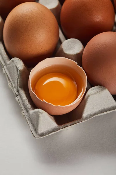 Broken eggshell with yellow yolk near eggs in carton box — Stock Photo