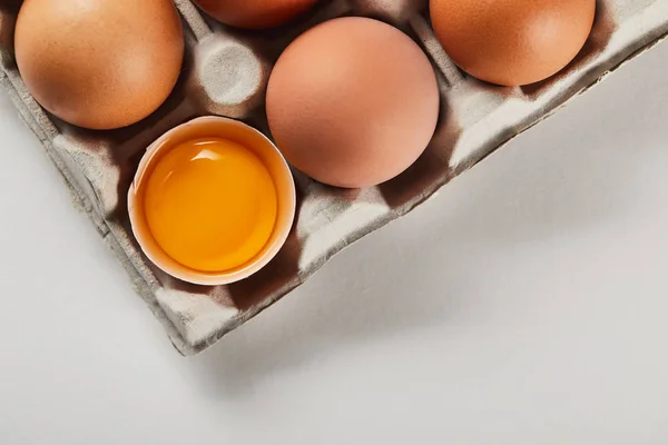 Vista superior de la cáscara de huevo rota con yema amarilla cerca de los huevos en caja de cartón - foto de stock