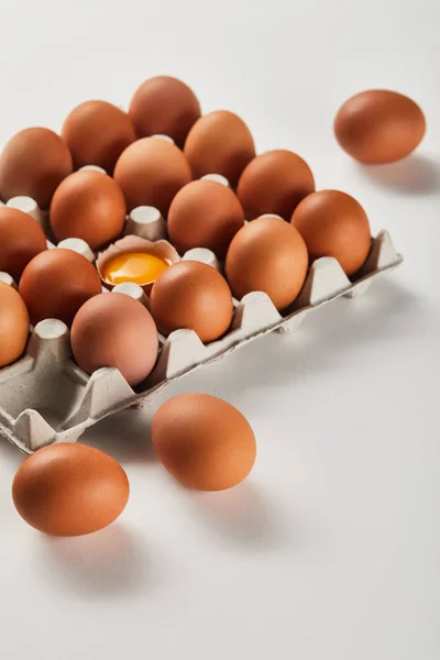 Broken eggshell with yellow yolk near eggs in carton box — Stock Photo