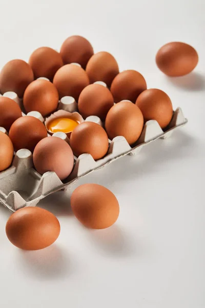 Cáscara de huevo rota con yema amarilla cerca de los huevos en caja de cartón - foto de stock