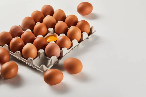 Broken eggshell with yellow yolk near eggs in carton box — Stock Photo