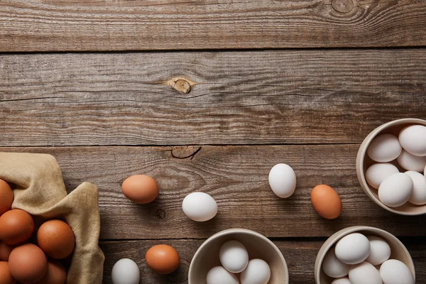 Vue du dessus des œufs de poulet dans des bols sur une table en bois avec du tissu — Photo de stock