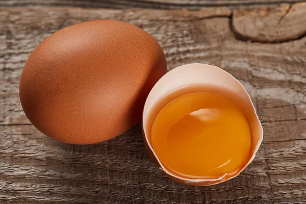 Broken eggshell with yellow yolk near egg on wooden table — Stock Photo