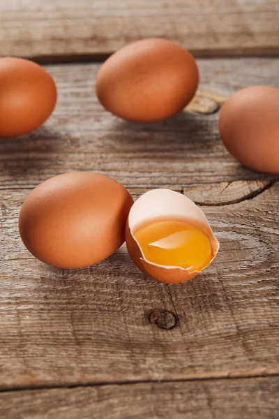 Zerbrochene Eierschale mit gelbem Eigelb in der Nähe von Eiern auf Holztisch — Stockfoto