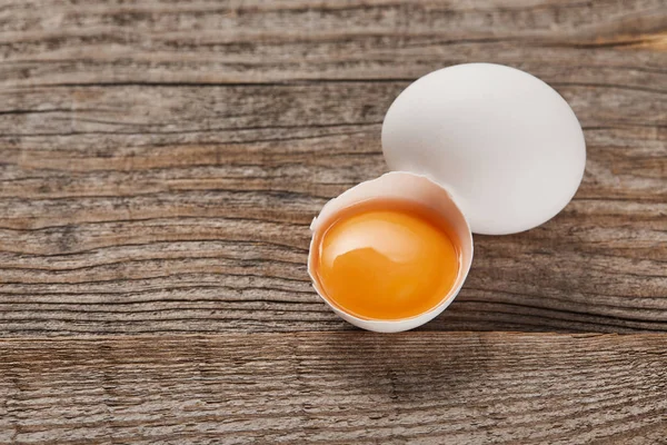 Broken eggshell with yellow yolk near egg on wooden table — Stock Photo