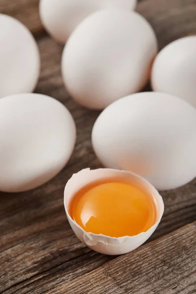 Selective focus of broken eggshell with yellow yolk near eggs on wooden table — Stock Photo