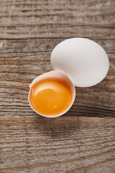 Cáscara de huevo rota con yema amarilla cerca del huevo en la mesa de madera - foto de stock