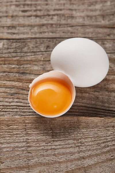 Broken eggshell with yellow yolk near egg on wooden table — Stock Photo
