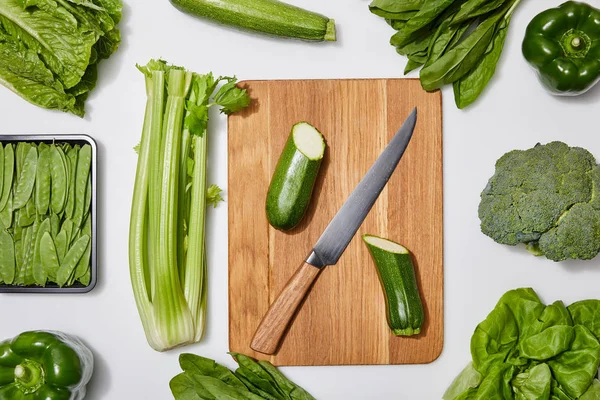 Top view of green vegetables and chopping board with knife on white background — Stock Photo