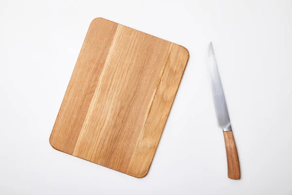 Vista superior de la tabla de cortar de madera vacía y cuchillo sobre fondo blanco - foto de stock