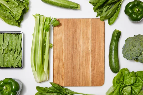 Vue du dessus des légumes verts autour de la planche à découper en bois sur fond blanc — Photo de stock