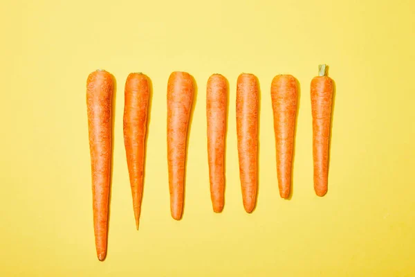 Vue du haut des carottes en rangée sur fond jaune — Photo de stock