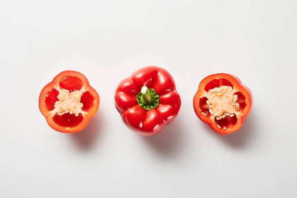 Top view of red organic cut and whole bell peppers on white background — Stock Photo