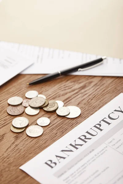 Selective focus of bankruptcy form, pen, coins and documents on brown wooden table — Stock Photo
