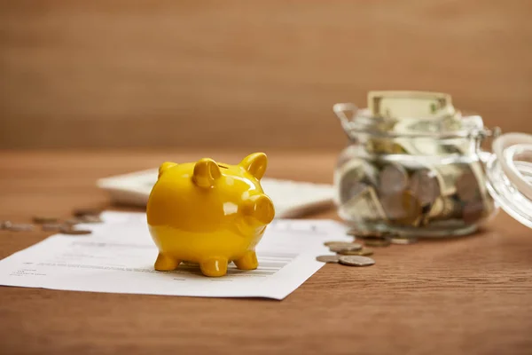 Selective focus of bankruptcy form, coins, yellow piggy bank and glass jar with dollar banknotes on wooden table — Stock Photo