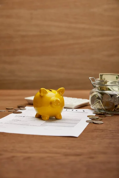 Foco seletivo da forma de falência, moedas, banco piggy amarelo, calculadora e frasco de vidro com notas de dólar na mesa de madeira — Fotografia de Stock