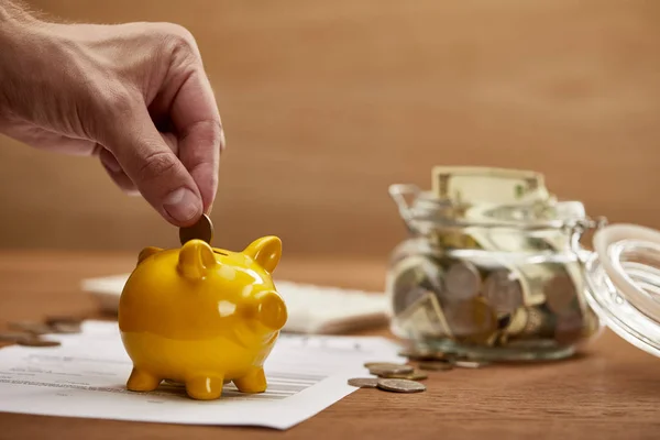 Cropped view of man putting coin in yellow piggy bank — Stock Photo