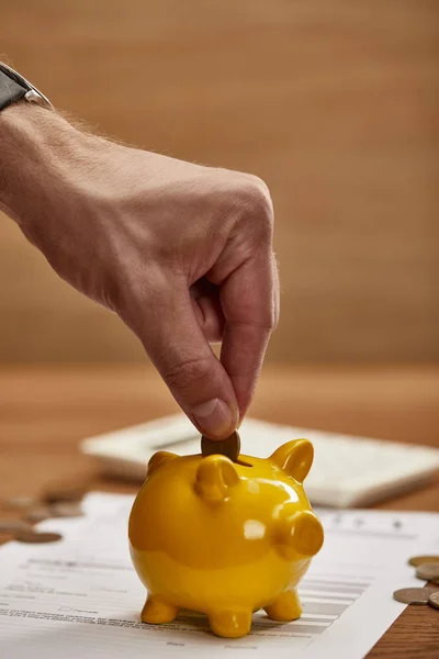 Partial view of man putting coin in yellow piggy bank — Stock Photo