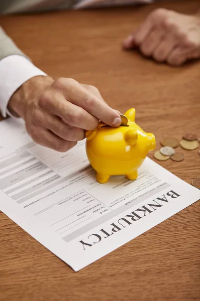 Visão cortada do homem colocando moeda no banco piggy amarelo na forma de falência — Fotografia de Stock