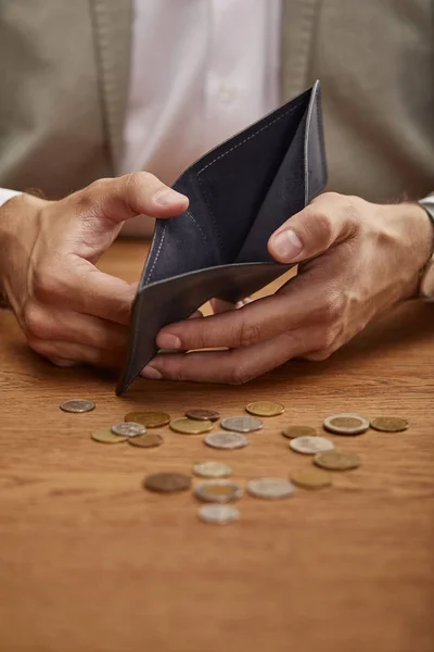 Vista recortada del hombre mostrando la cartera vacía cerca de las monedas en la mesa de madera - foto de stock