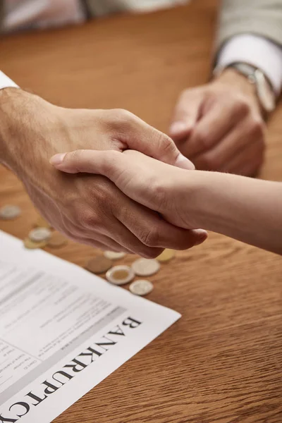 Cropped view of man and woman shaking hands near bankruptcy form — Stock Photo