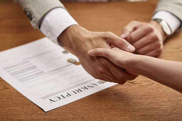 Partial view of man and woman shaking hands near bankruptcy form — Stock Photo