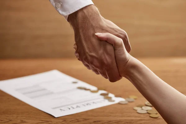 Enfoque selectivo del hombre y la mujer estrechando manos cerca de la forma de bancarrota y monedas - foto de stock