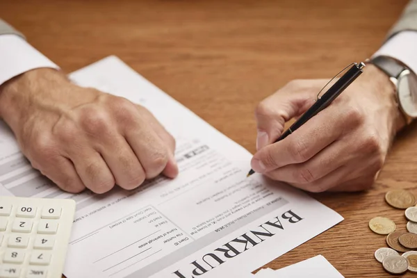 Cropped view of man filling in bankruptcy form at wooden table — Stock Photo