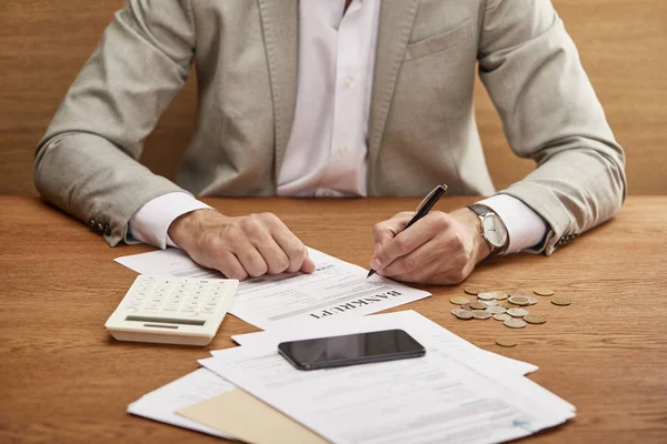 Обрезанный взгляд бизнесмена в костюме, заполняющего форму банкротства за деревянным столом — стоковое фото