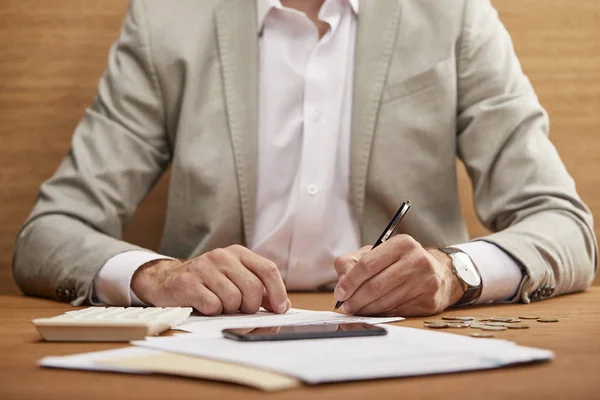 Vue partielle de l'homme d'affaires en costume remplissant le formulaire de faillite à la table en bois — Photo de stock