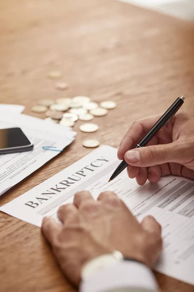 Cropped view of businessman in suit  filling in bankruptcy form at wooden table with coins — Stock Photo