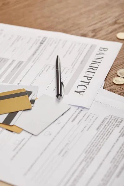 Enfoque selectivo de la forma de bancarrota entre los documentos, tarjetas de crédito y monedas en la mesa de madera - foto de stock