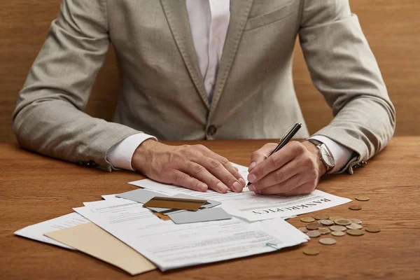 Vista parcial del hombre de negocios en traje llenando formulario de bancarrota en la mesa de madera con documentos y tarjetas de crédito - foto de stock