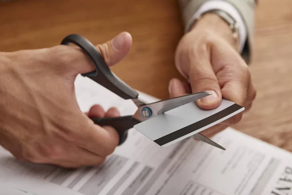 Partial view of businessman cutting credit card with scissors at wooden table — Stock Photo