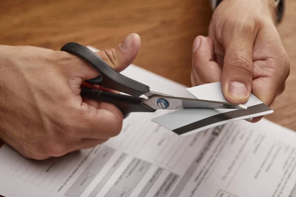 Cropped view of businessman cutting credit card with scissors at wooden table — Stock Photo