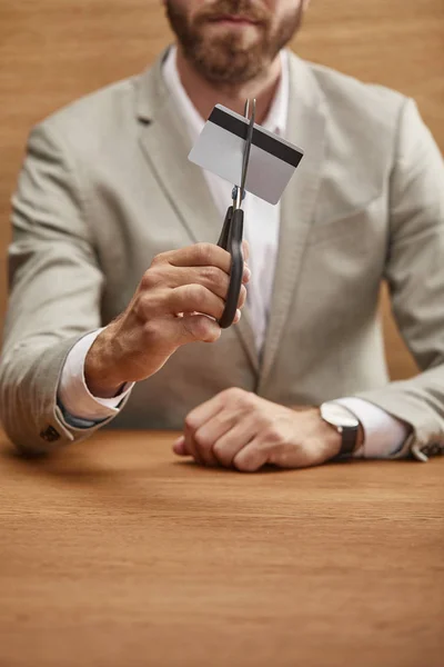 Foyer sélectif de barbu homme d'affaires en costume tenant carte de crédit avec ciseaux à la table en bois — Photo de stock